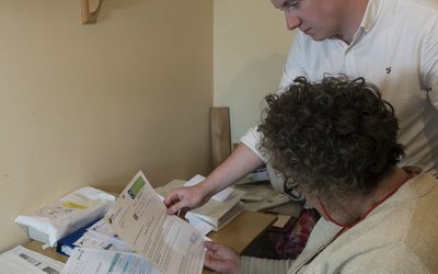 Man explaining bills to a seated woman.