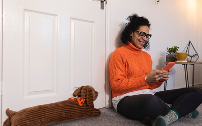 Woman sitting on the floor at home with a draught excluder by the door.